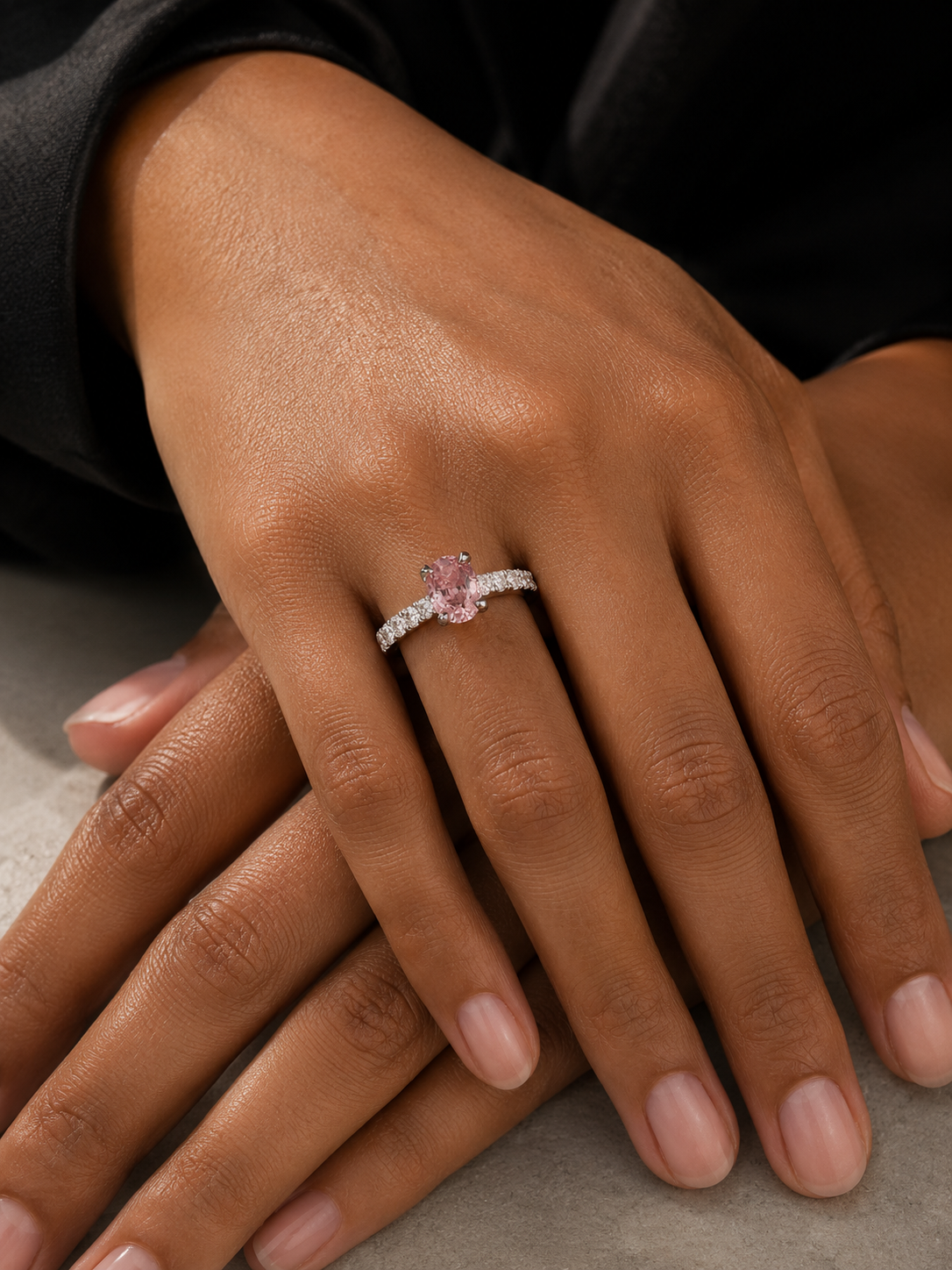 Close-up of a hand wearing a pink gemstone ring on a neutral background